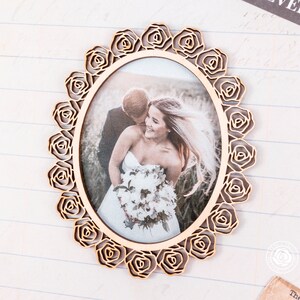 May include: A wooden picture frame with a rose design. The frame is oval shaped and has a photo of a bride and groom inside. The photo shows the couple in a field with a bouquet of flowers.