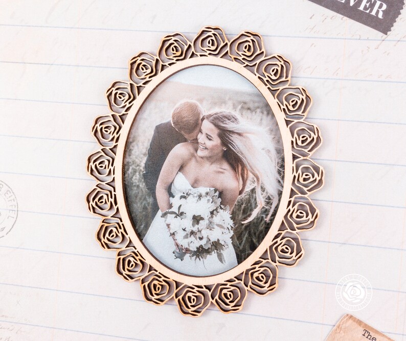 May include: A wooden picture frame with a rose design. The frame is oval shaped and has a photo of a bride and groom inside. The photo shows the couple in a field with a bouquet of flowers.