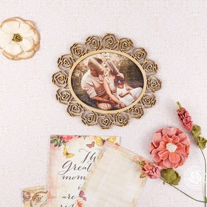 May include: A wooden picture frame with a floral design, featuring a photo of a family of three. The frame is decorated with a gold finish and has a white background. The photo shows a couple and their child, with the parents looking at each other and the child looking at the camera. The photo is set against a backdrop of green trees and foliage.