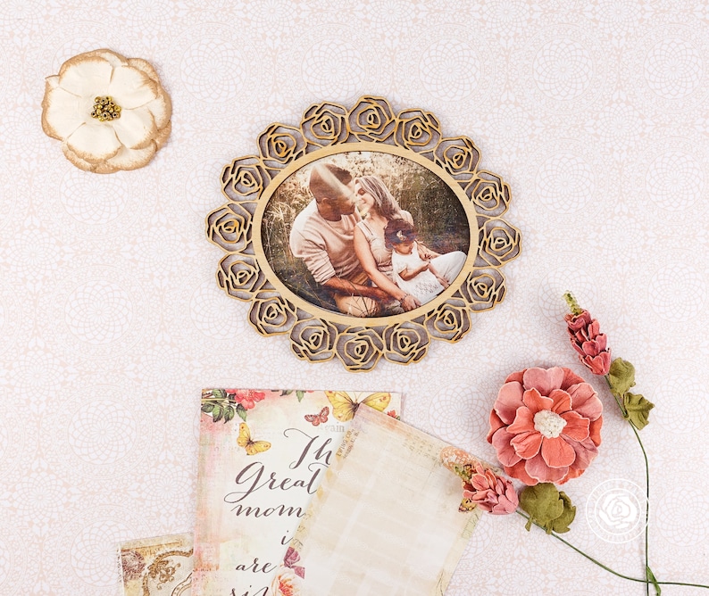 May include: A wooden picture frame with a floral design, featuring a photo of a family of three. The frame is decorated with a gold finish and has a white background. The photo shows a couple and their child, with the parents looking at each other and the child looking at the camera. The photo is set against a backdrop of green trees and foliage.