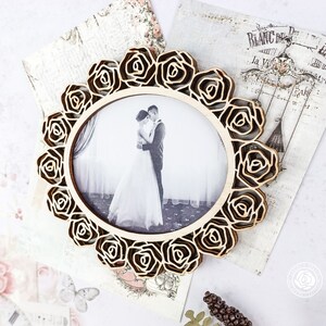 May include: A wooden picture frame with a decorative rose design. The frame is holding a black and white photo of a couple.
