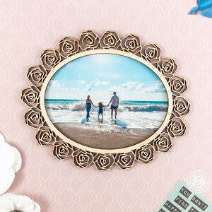 May include: A wooden photo frame with a rose design. The frame is holding a photo of a family of three on a beach.