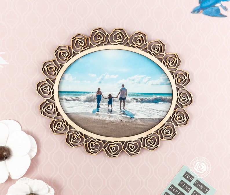 May include: A wooden photo frame with a rose design. The frame is holding a photo of a family of three on a beach.