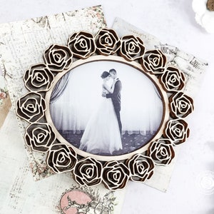 May include: A wooden picture frame with a decorative design of roses surrounding a photo of a couple. The photo shows a bride and groom embracing.
