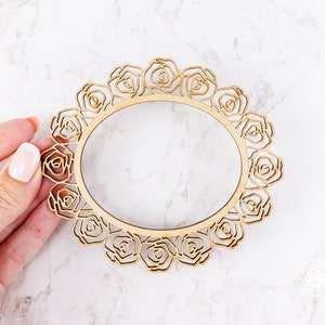 May include: A wooden frame with a decorative design of roses. The frame is circular and has a cutout in the center.