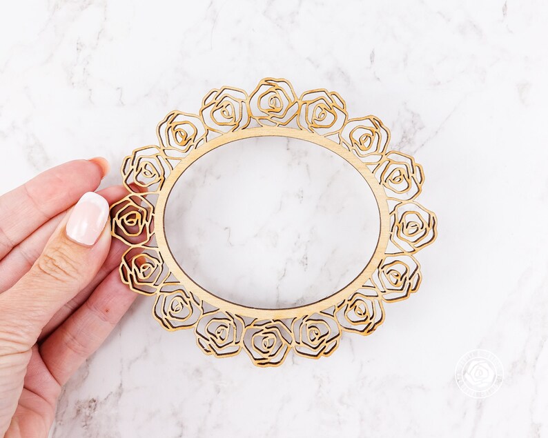 May include: A wooden frame with a decorative design of roses. The frame is circular and has a cutout in the center.