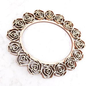 May include: A wooden round frame with a decorative design of roses around the edge. The frame is made of light brown wood and has a natural finish.