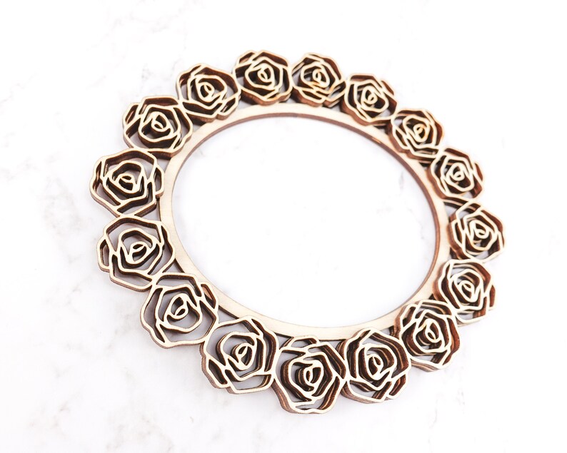 May include: A wooden round frame with a decorative design of roses around the edge. The frame is made of light brown wood and has a natural finish.