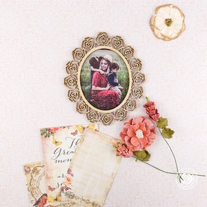 May include: A gold oval-shaped picture frame with a floral design. The frame contains a photo of a woman and two children. The photo is set against a green background. The frame is surrounded by pink and white flowers.