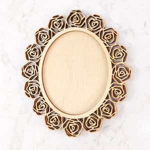 May include: A wooden oval frame with a decorative rose design. The frame is made of light brown wood and has a smooth finish.