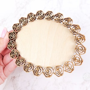 May include: A round wooden plaque with a decorative border of laser-cut roses. The plaque is light brown and the roses are a darker brown.