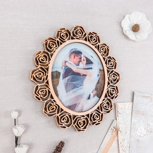 May include: A wooden photo frame with a rose design, featuring a wedding photo of a couple in a white dress and a suit.
