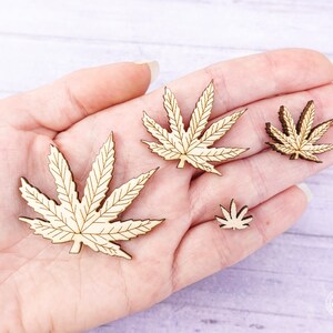 Puede incluir: Cuatro formas de hojas de madera en forma de hojas de marihuana. Las hojas son de diferentes tama&ntilde;os y se sostienen en una mano.