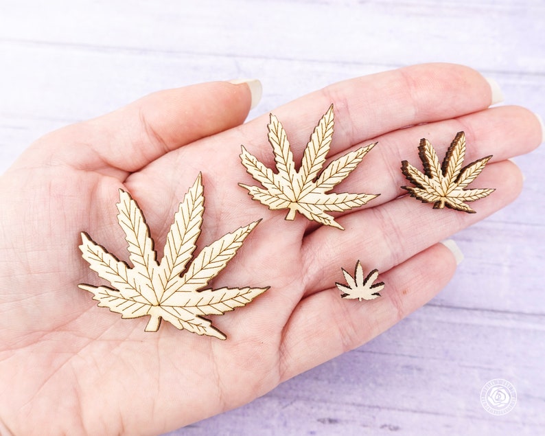 Puede incluir: Cuatro formas de hojas de madera en forma de hojas de marihuana. Las hojas son de diferentes tama&ntilde;os y se sostienen en una mano.