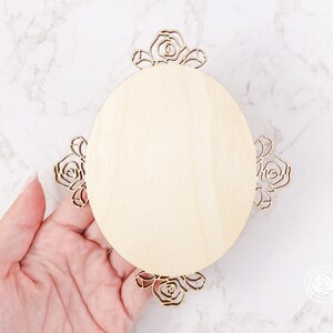 May include: A round wooden plaque with a decorative floral design around the edge. The plaque is unfinished and ready to be painted or stained.