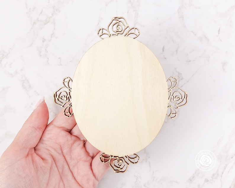 May include: A round wooden plaque with a decorative floral design around the edge. The plaque is unfinished and ready to be painted or stained.