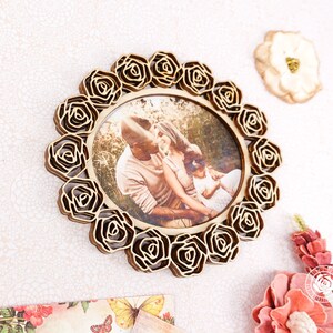 May include: A wooden photo frame with a decorative rose design. The frame holds a photo of a family of three.
