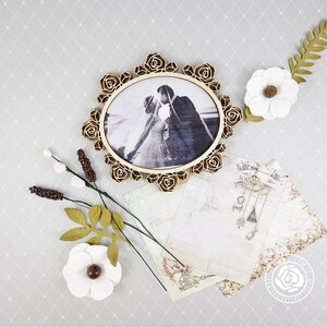 Puede incluir: Un marco de madera de color dorado con un dise&ntilde;o floral en relieve rodea una fotograf&iacute;a en blanco y negro de una pareja. El marco est&aacute; sobre un fondo blanco con un patr&oacute;n floral.
