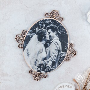 May include: A wooden oval frame with a black and white photo of a couple kissing. The frame is decorated with carved roses around the edge.