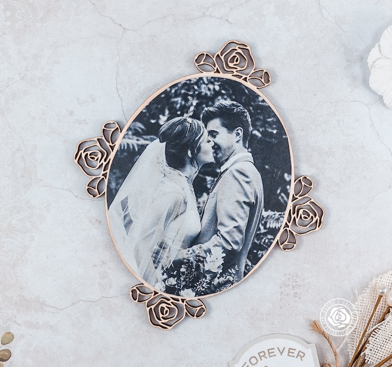 May include: A wooden oval frame with a black and white photo of a couple kissing. The frame is decorated with carved roses around the edge.