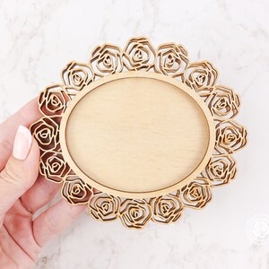 May include: A wooden round frame with a decorative rose design. The frame is unfinished and ready to be painted or stained.