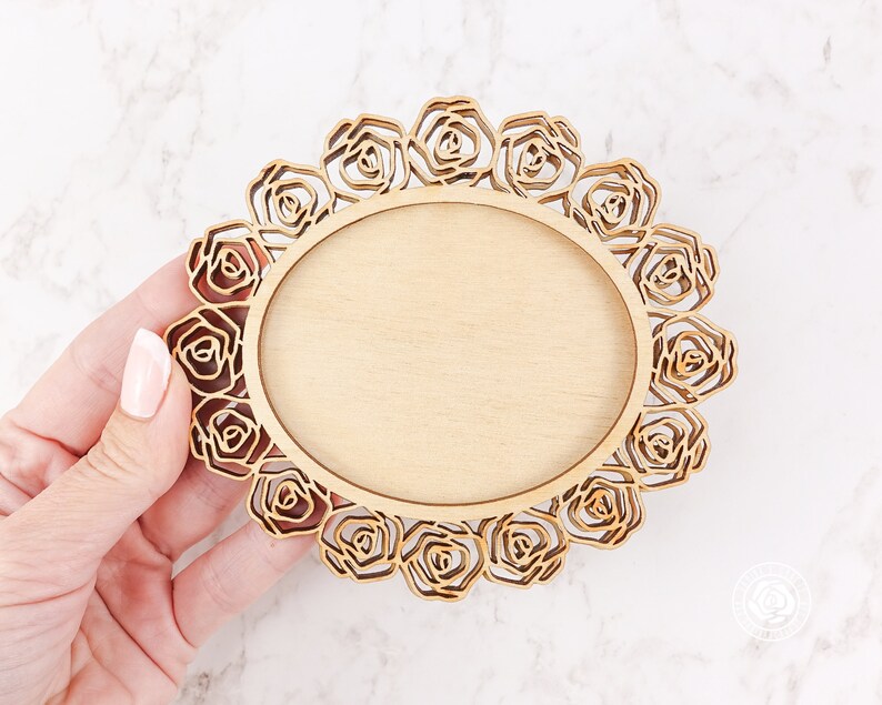 May include: A wooden round frame with a decorative rose design. The frame is unfinished and ready to be painted or stained.