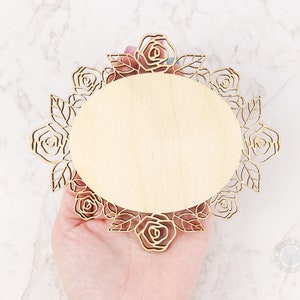 May include: A wooden round plaque with a decorative laser cut design of roses and leaves around the edge. The plaque is blank and ready to be personalized.