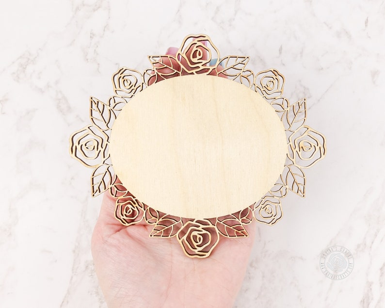 May include: A wooden round plaque with a decorative laser cut design of roses and leaves around the edge. The plaque is blank and ready to be personalized.