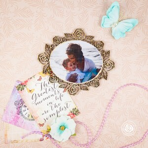 May include: A gold-toned decorative frame with a photo of a mother and child. The frame is surrounded by roses and leaves. The photo is set against a light blue background. The text "The greatest moments in life are the simplest" is written on a card with floral designs.