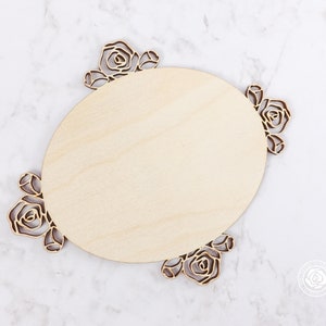 May include: A wooden oval sign with a decorative rose design around the edge. The sign is blank and ready to be personalized.