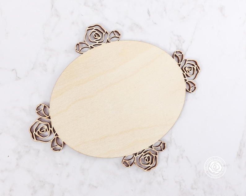 May include: A wooden oval sign with a decorative rose design around the edge. The sign is blank and ready to be personalized.