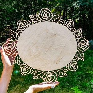 May include: A wooden round sign with a decorative floral border of roses and leaves. The sign is blank and ready to be personalized.