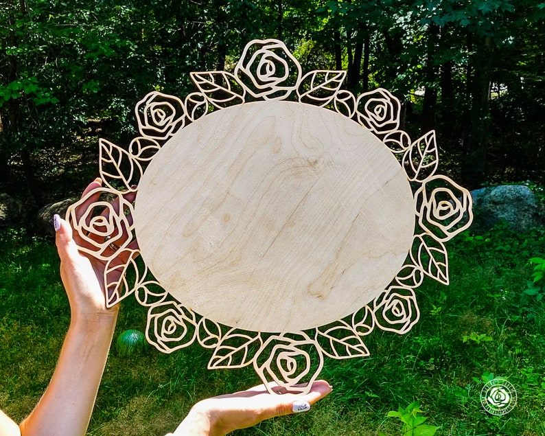 May include: A wooden round sign with a decorative floral border of roses and leaves. The sign is blank and ready to be personalized.