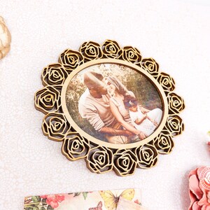 May include: A wooden photo frame with a circular design featuring a decorative border of roses. The frame holds a photo of a family of three in a natural setting.