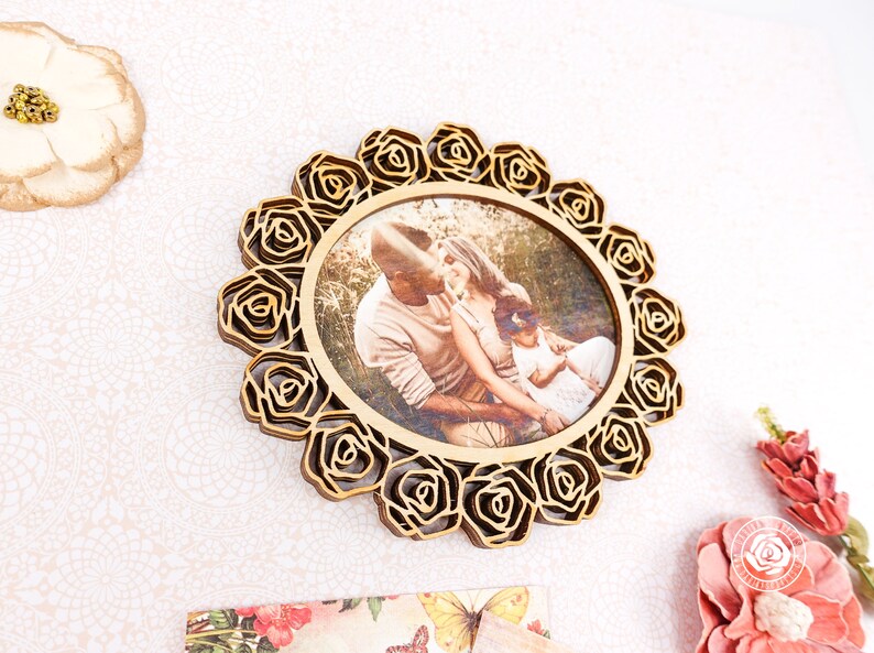 May include: A wooden photo frame with a circular design featuring a decorative border of roses. The frame holds a photo of a family of three in a natural setting.
