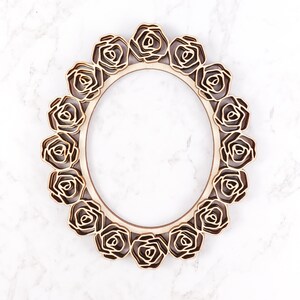 May include: A wooden oval frame with a decorative design of roses around the perimeter. The frame is made of light brown wood and has a natural finish.