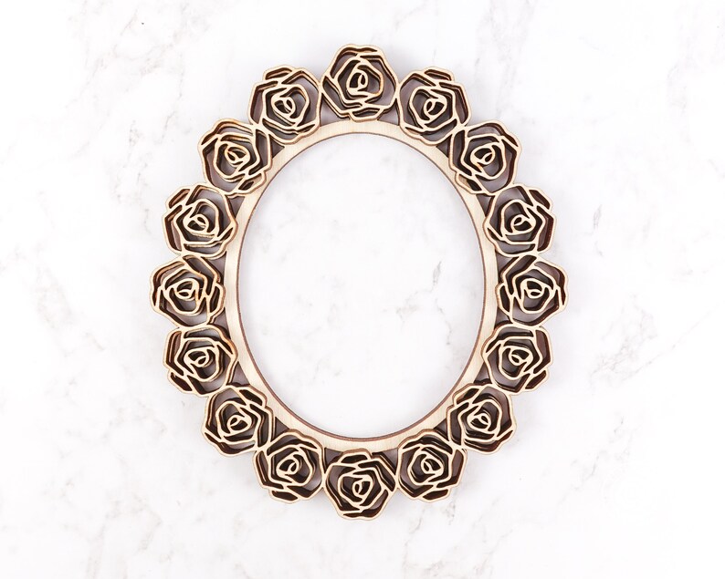 May include: A wooden oval frame with a decorative design of roses around the perimeter. The frame is made of light brown wood and has a natural finish.