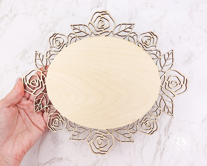 May include: A wooden oval-shaped plaque with a decorative rose design around the edge. The plaque is made of light wood and has a natural finish.