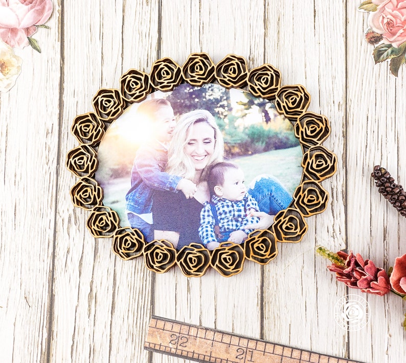 May include: A wooden picture frame with a rose design, featuring a photo of a mother and her two children. The frame is a light brown colour and has a circular shape.
