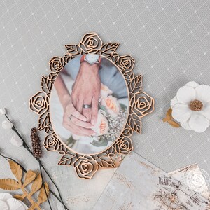 May include: A wooden picture frame with a rose design, featuring a photo of a couple's hands holding a bouquet of flowers. The frame is a light brown color and has a rustic look.