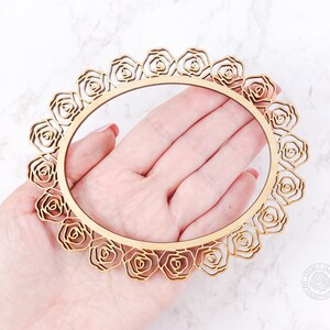 May include: A wooden circle frame with a decorative rose design. The frame is made of natural wood and has a delicate, intricate pattern.