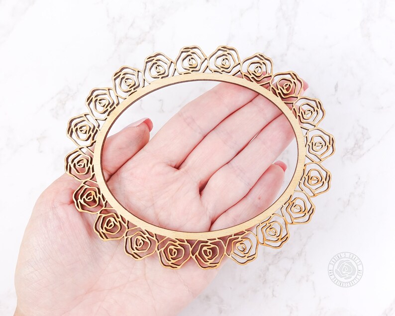 May include: A wooden circle frame with a decorative rose design. The frame is made of natural wood and has a delicate, intricate pattern.