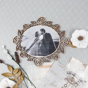 May include: A wooden photo frame with a decorative rose design. The frame is holding a black and white photo of a bride and groom.