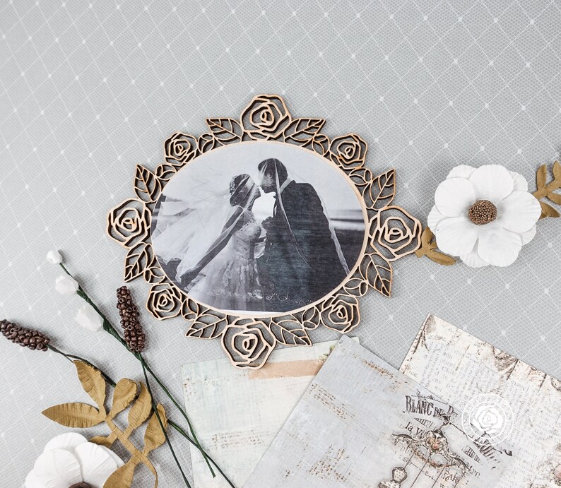 May include: A wooden photo frame with a decorative rose design. The frame is holding a black and white photo of a bride and groom.