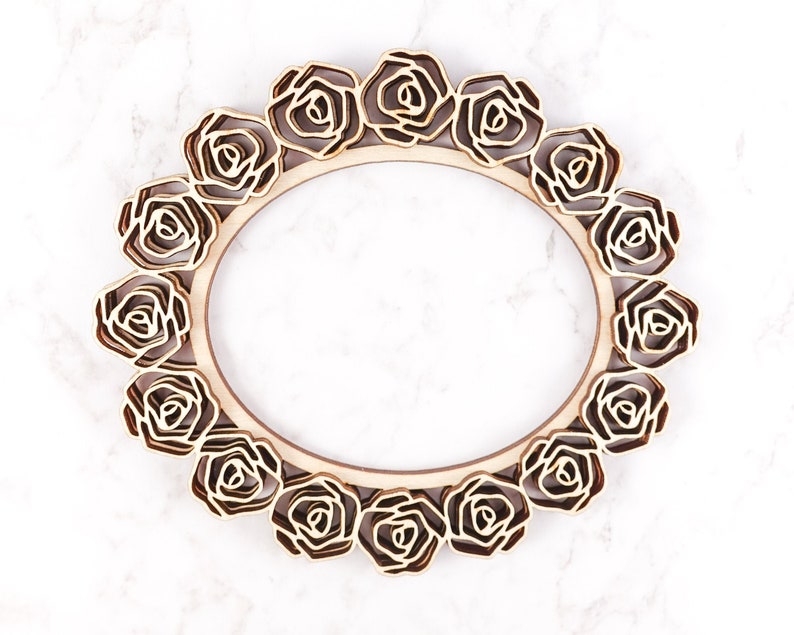 May include: A wooden frame with a decorative design of roses around the perimeter. The frame is light brown and has a natural wood finish.