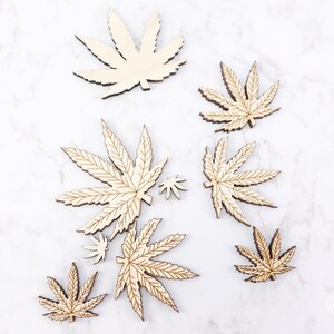 Puede incluir: Un conjunto de ocho recortes de hojas de cannabis de madera en varios tama&ntilde;os. Las hojas son todas de color madera natural y tienen un acabado liso.