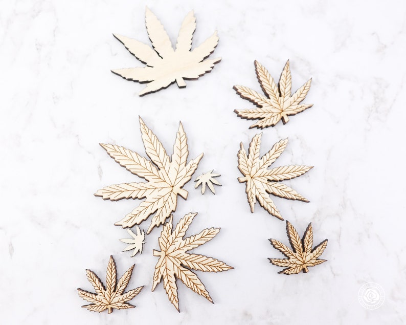 Puede incluir: Un conjunto de ocho recortes de hojas de cannabis de madera en varios tama&ntilde;os. Las hojas son todas de color madera natural y tienen un acabado liso.