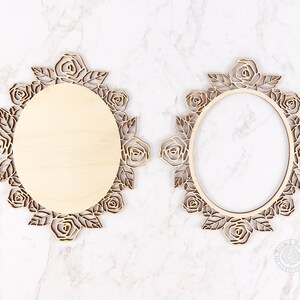 May include: Two wooden oval frames with intricate rose and leaf cutouts. One frame has a solid wooden center, while the other is open. The frames are light brown and sit on a white marble surface. The frames are decorative.