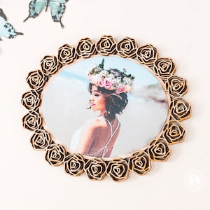 May include: A wooden photo frame with a circular cutout and a floral design. The frame is made of light brown wood and has a gold finish. The floral design is made up of roses that are arranged in a circle around the cutout. The frame is ideal for displaying a photo of a loved one.