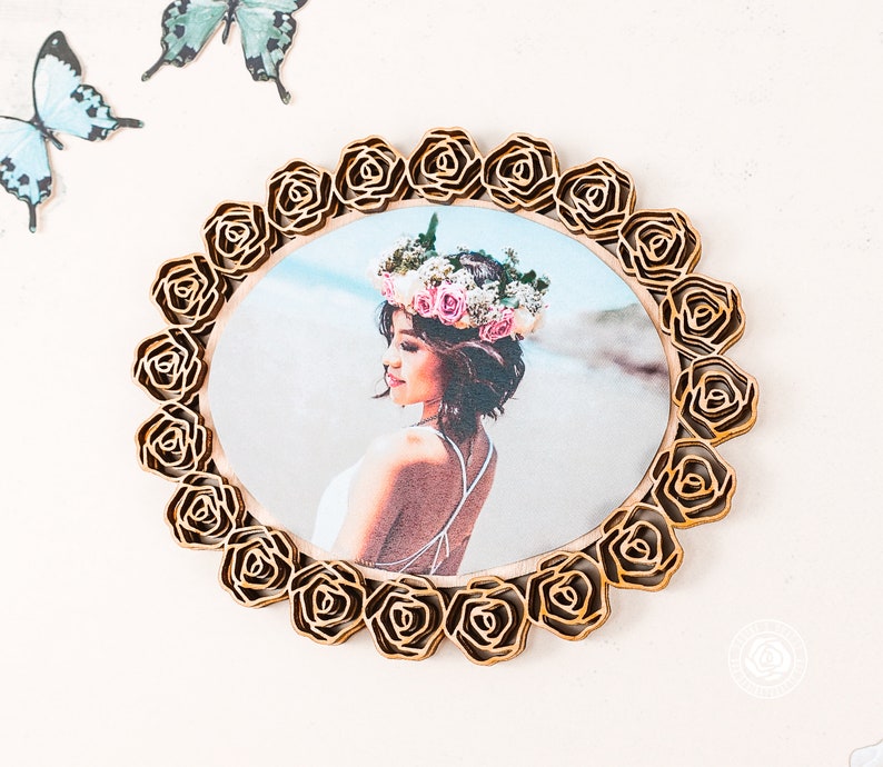 May include: A wooden photo frame with a circular cutout and a floral design. The frame is made of light brown wood and has a gold finish. The floral design is made up of roses that are arranged in a circle around the cutout. The frame is ideal for displaying a photo of a loved one.